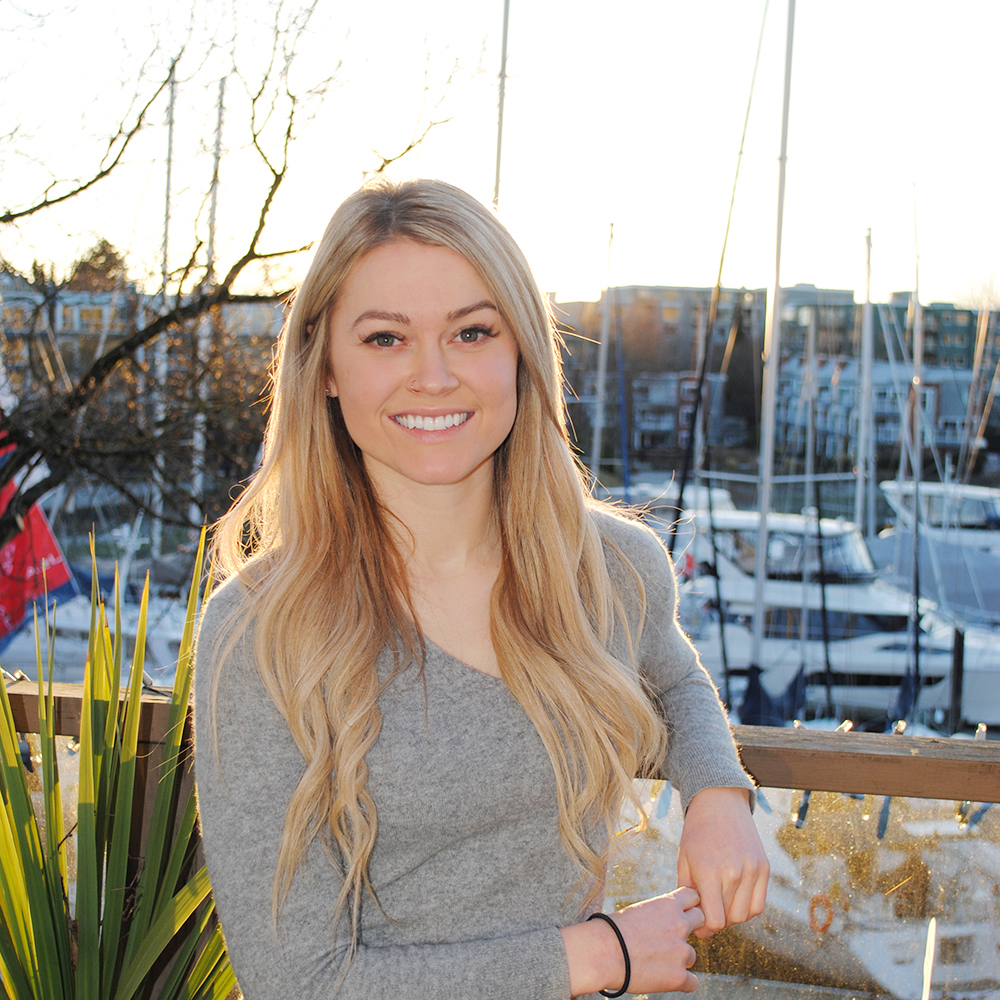 Tara Nay Headshot A headshot photo of Tara Nay, a Speech-Language Pathologist at Granville Island Speech. She stands outside of the clinic with boats and the pier in the background.