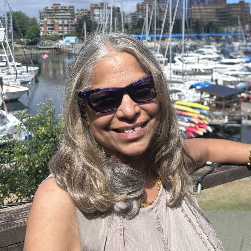 A headshot photo of Vinni Panikkar outside of the Granville Island Speech clinic. There are boats and the Granville Island pier in the background.