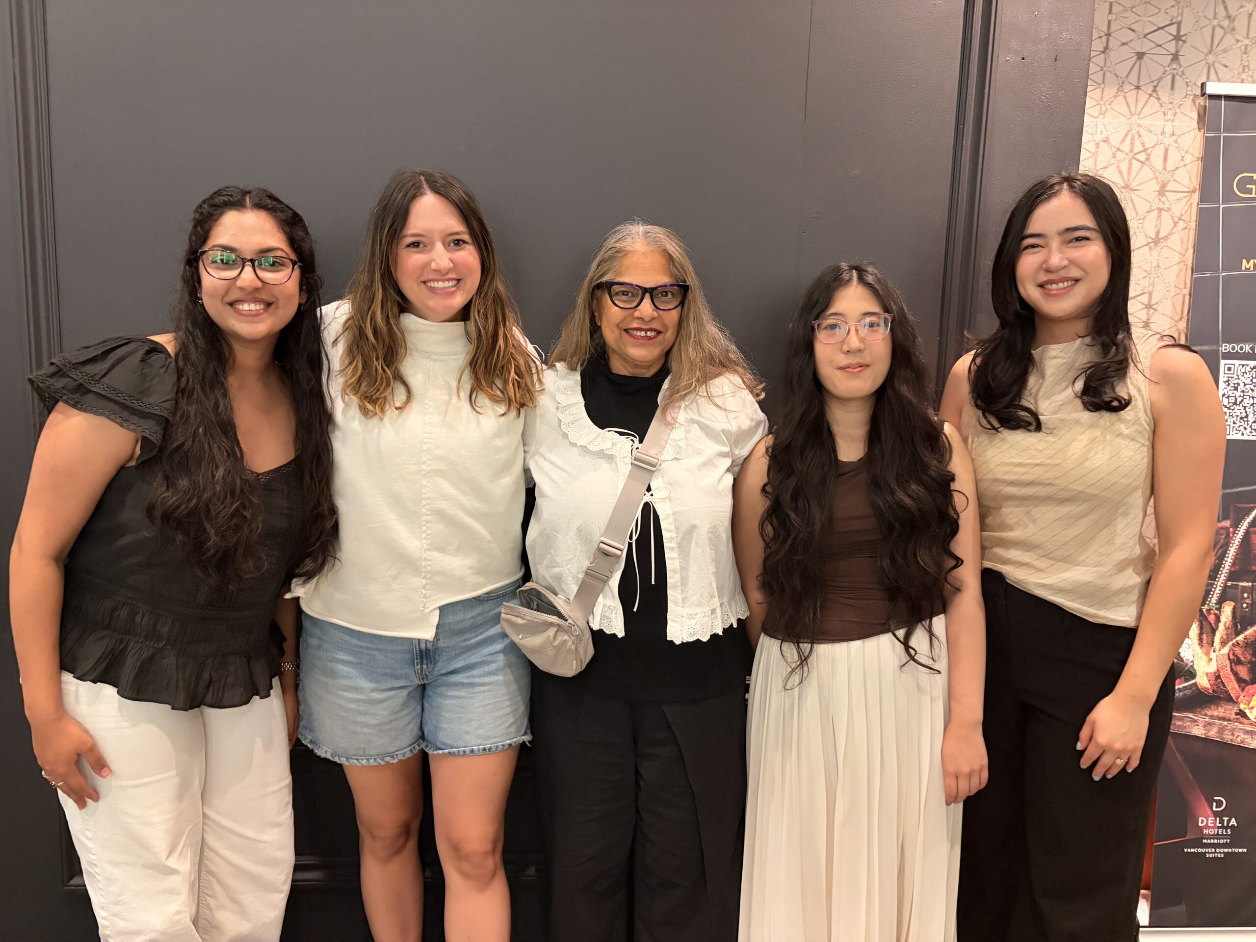 A photo of Vinni with her team standing against a black wall. 